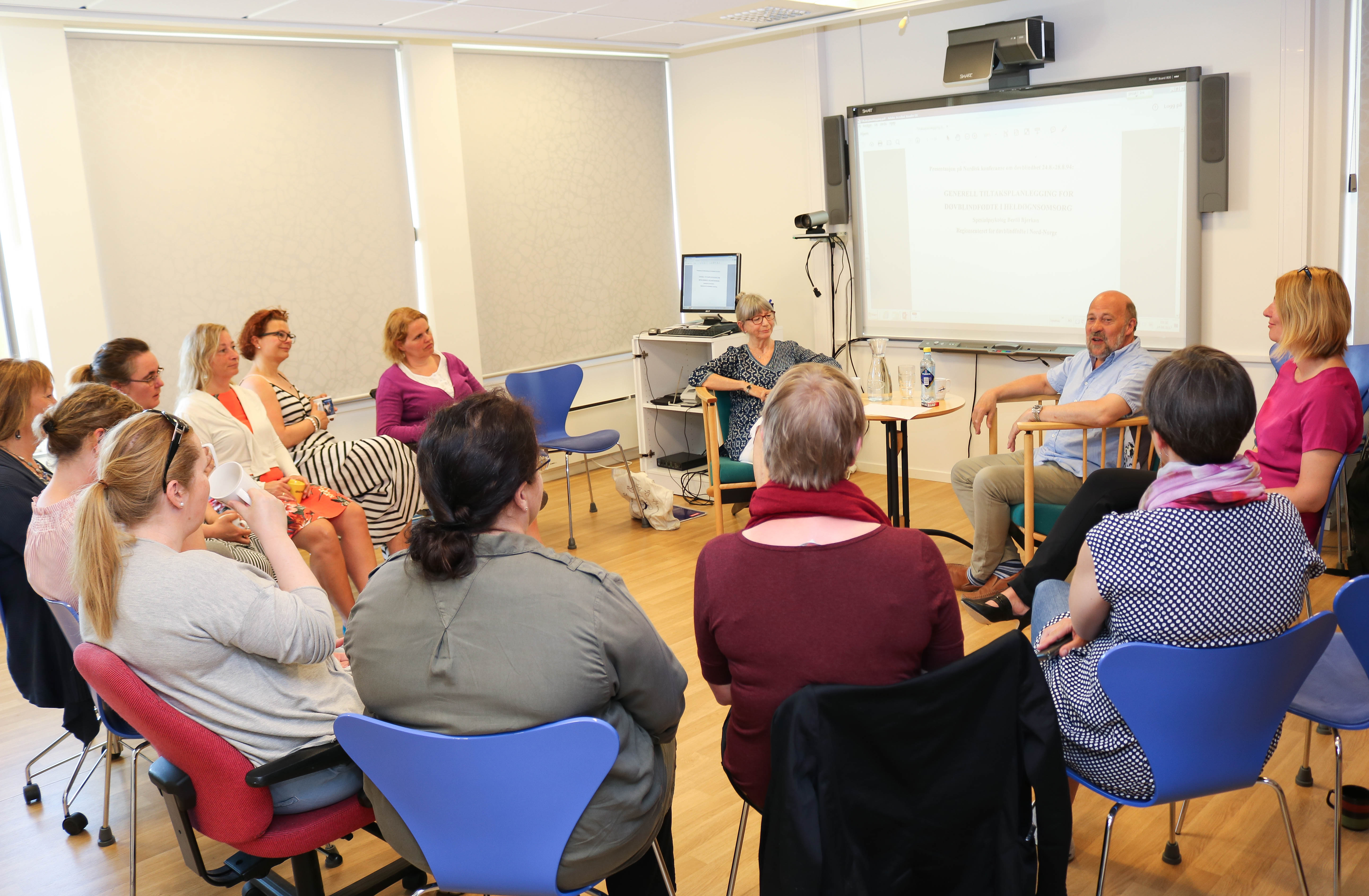 En gruppe med kvinner fra Regionsenteret for døvblinde i Tromsø sitter rundt Bertil Bjerkan i VK-rommet. 