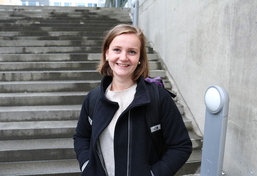 En smilende Ida skredlund med hendene i lomma foran betongtrappene ved Tromsø bibliotek og byarkiv.