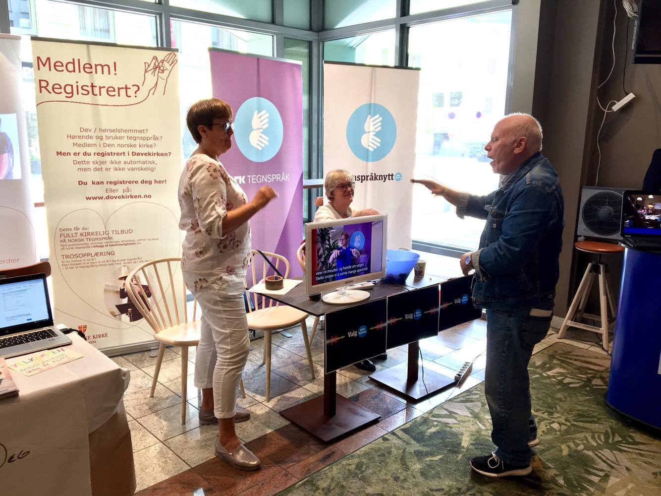 NRK-tegnspråk sin stand. En eldre mann diskuterer med to kvinner fra NRK-tegnspråk.