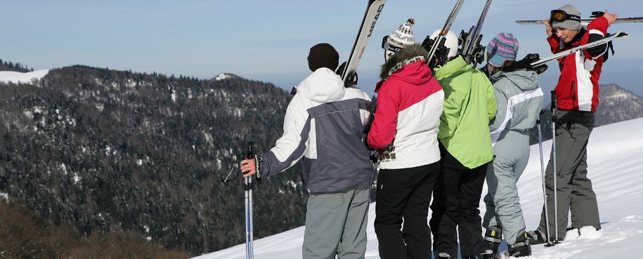Bilde av ungdom som står med slalomutstyr og ser utover en snødekt bakke i skogen