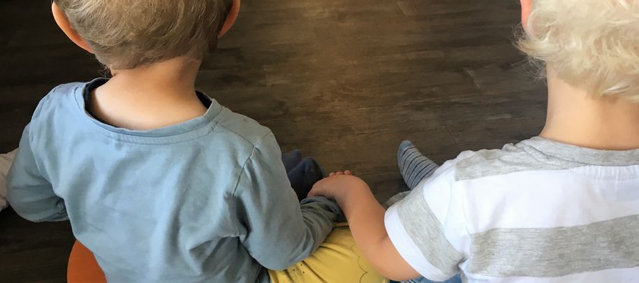 Bilde av to barn som sitter med ryggen til, og holder hender