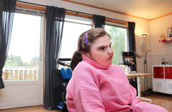 Jeg med CHARGE syndrom sitter i rullestol i sin egen stue. Hun er medfødt døvblind.