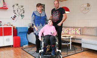 Victoria Elise Mo sammen med sine foreldre i hennes egen bolig. Foto: Roy-Morten Østerbøl. Mor og far står bak deres datter i rullestol, hun har CHARGE syndrom og de er i hennes egen stue.