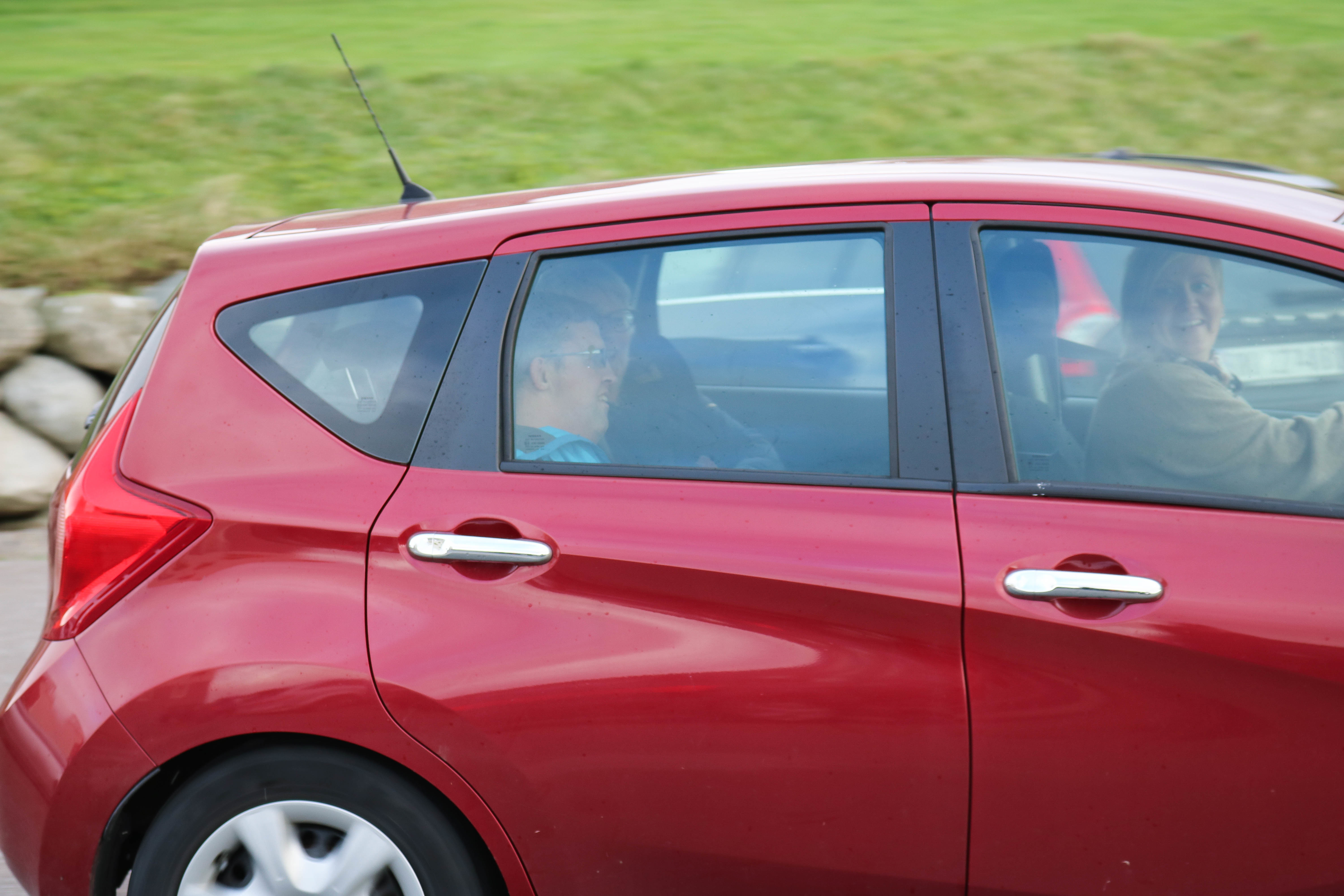 Tre personer kan skimtes inne i en rød bil. 