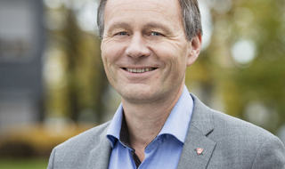 Foto: Vestfold fylkeskommune. Portrettbilde av smilende mann med blå skjorte og grå dressjakke.