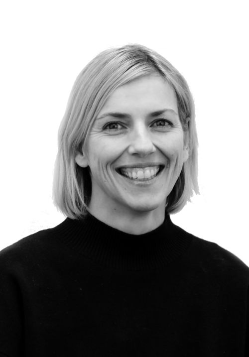 Foto av Eikholt. Smilende kvinne med lyst, halv langt hår. Hun har på seg en mørk genser.