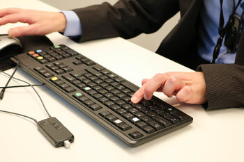 Døvblind mann skriver på tilpasset datatastatur. En lyd- og taleforsterker ligger i forkant av tastaturet.