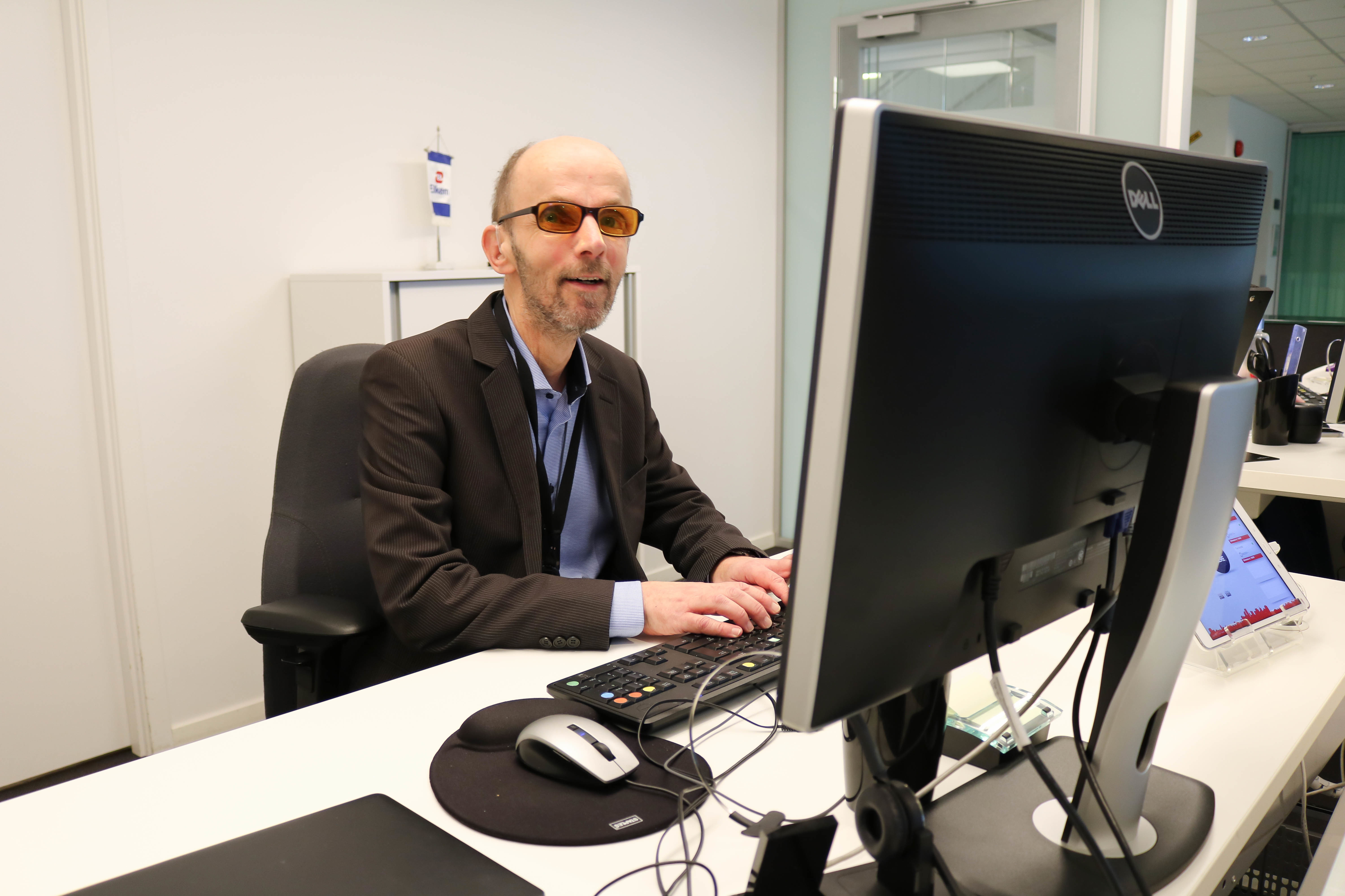 Døvblind mann med oransje filterbriller sitter på sin kontorplass og jobber med data. 