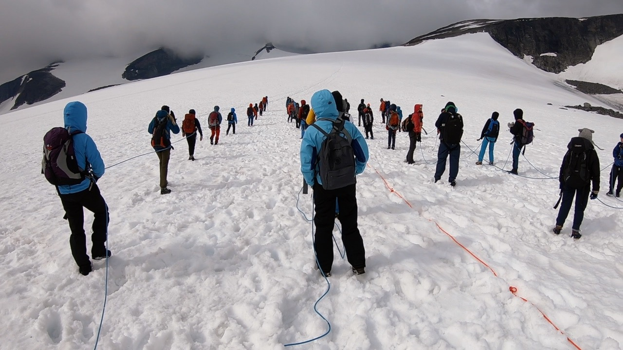 Mennesker som går over en isbre på vei opp til Galdhøpiggen. De er sikret med tau.