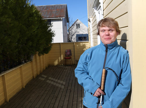Denis Protiuc ved sitt hjem i Brønnøysund. Foto: Roy-Morten Østerbøl. Portrettbilde av døvblind mann ved gul husvegg. Han har på seg en lyseblå fleecejakke og holder en blindestokk mot sin mage.