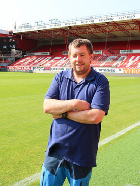 Roy-Morten Østerbøl Mann i blå piquet poserer inne på Brann stadion i Bergen, han holder armene i kors.