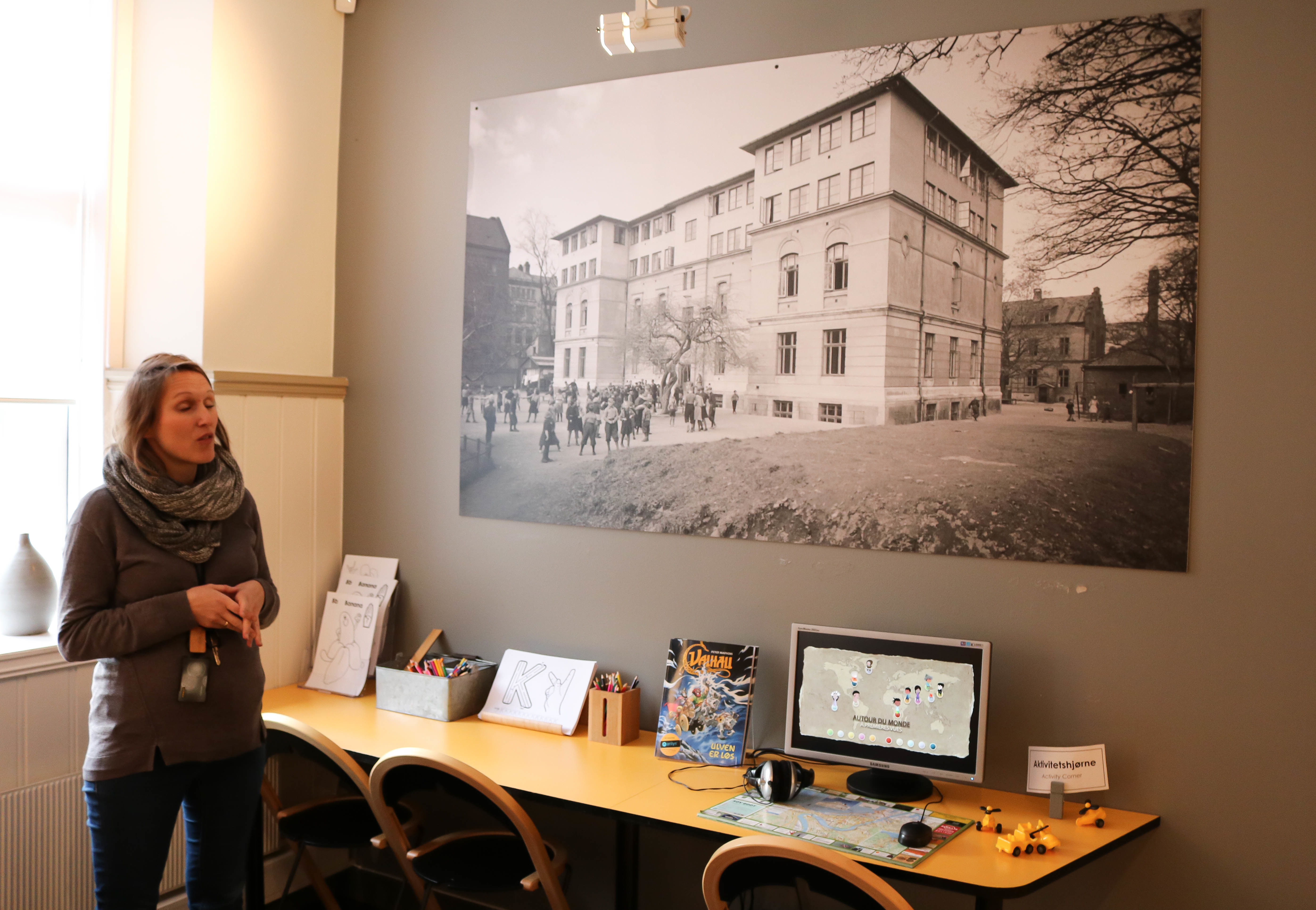  Kvinne forteller om eldre bygning, avbildet på et stort sort-hvitt fotografi, som henger på vegg.