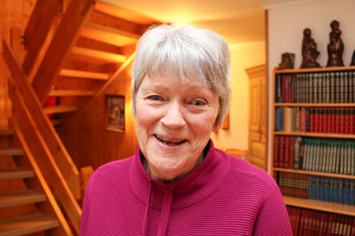 Kari Engan hjemme hos seg selv i Trondheim. Foto: Roy-Morten Østerbøl. Kvinne i rød-lilla genser står foran vegg-til-veggseksjonen i sin stue.