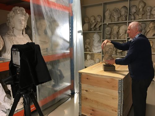 Eldre døvblind mann undersøker et marmorhode i rom med en rekke skulpturer.