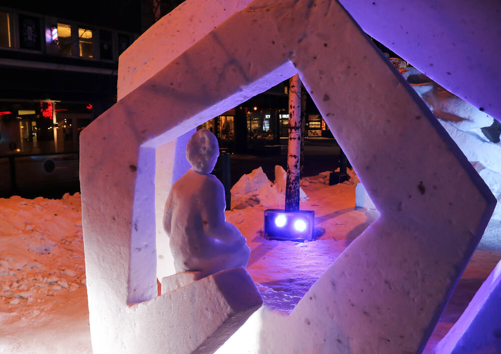Menneskelignende snøskulptur "ser" mot en boks med to lys.