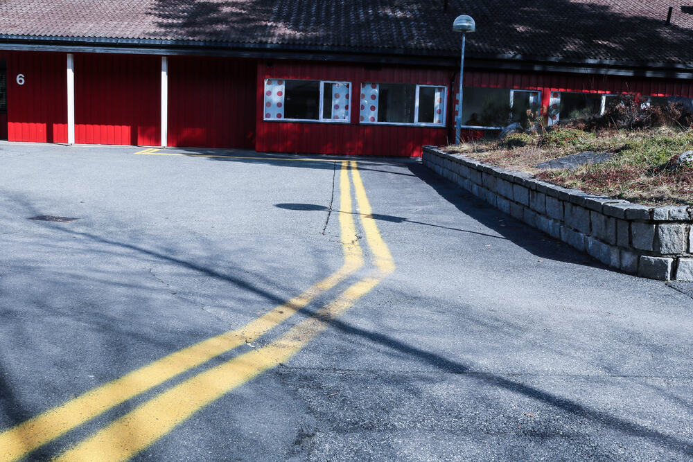 Eikholt, gule ledestriper på asfalt mot rød bygning.