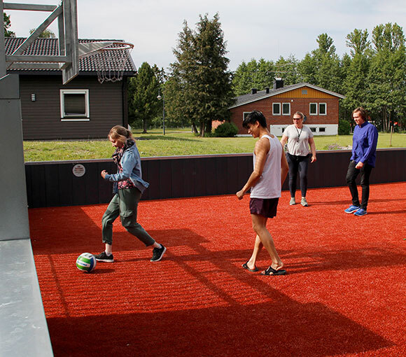 Fire personer spiller fotball på universelt utformet ballbinge. 
