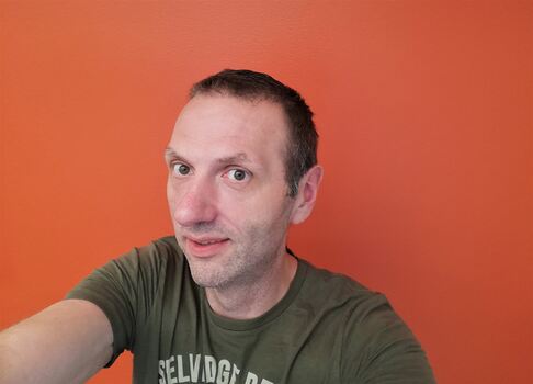 Mann tar selfi med oransje bakgrunnsvegg.