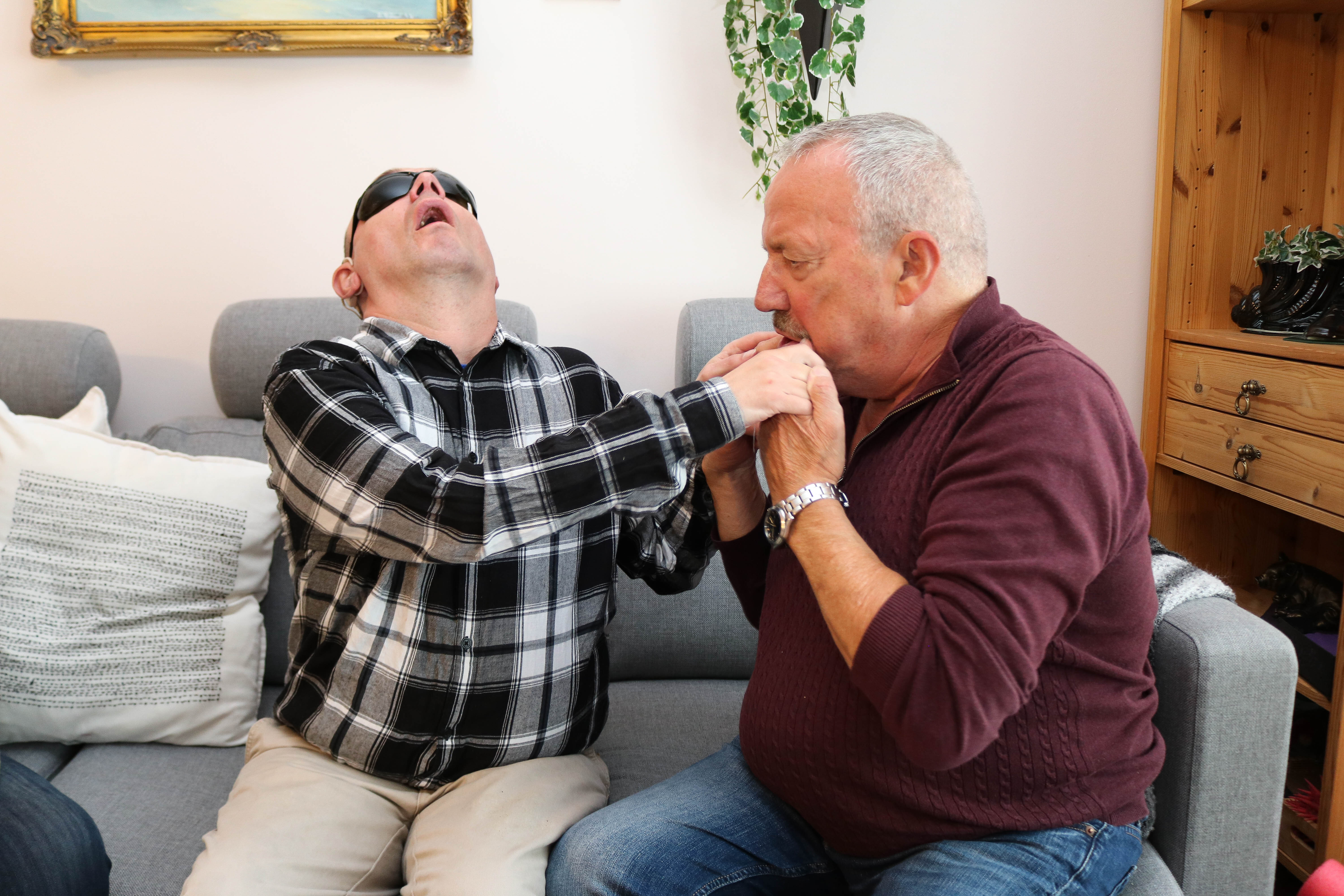 Mann kommuniserer med sin voksne døvblinde sønn gjennom taktile tegn. 