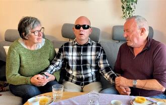 Døvblind mann sammen med sine foreldre i en sofa, far til høyre og mor til venstre.