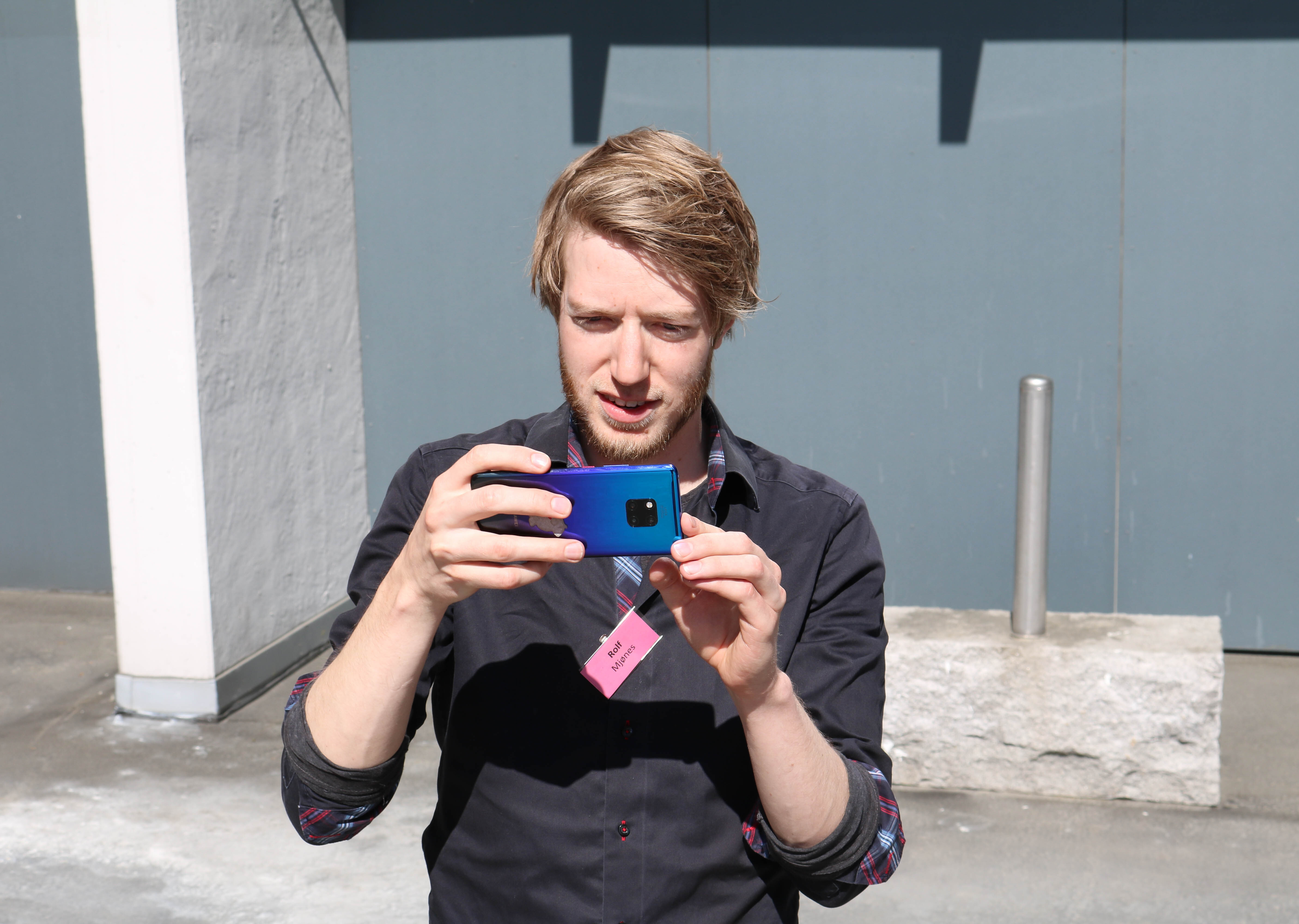 Mann tar bilde med sin mørkeblå mobiltelefon. 