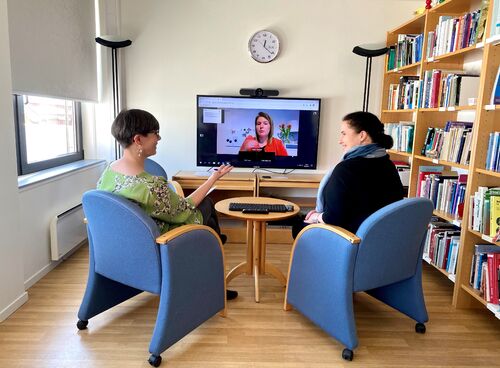 To kvinner sitter på et møterom og følger et webinar på en større tv-skjerm.