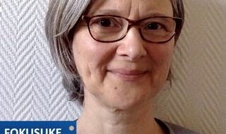 Portrettbilde av kvinne med briller, fokusukelogo nede til venstre.