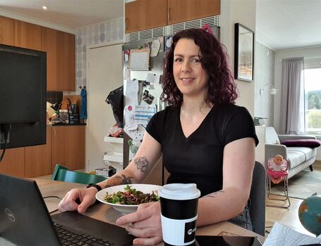 Kvinne på hjemmekontor. Hun sitter på kjøkkenet sitt, spiser salat og jobber samtidig med laptopen sin.