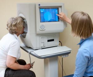 Testpersonen kikker inn i et apparat. Undersøkeren avleser en dataskjerm plassert på siden av apparatet. 