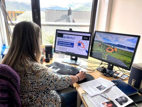 Kvinne på sitt kontor, hun følger med på et fagwebinar via to PC-skjermer.
