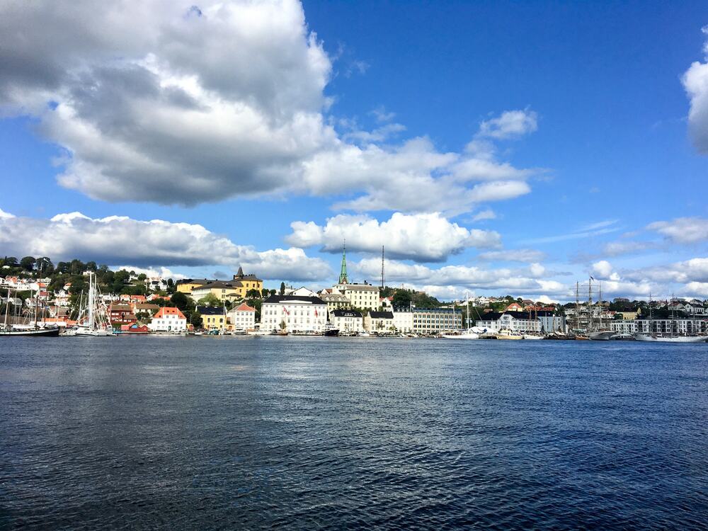 Norsk by sett fra sjøsiden, blå himmel og tykke gråhvite skyer over byen som ligger på Sørlandet.