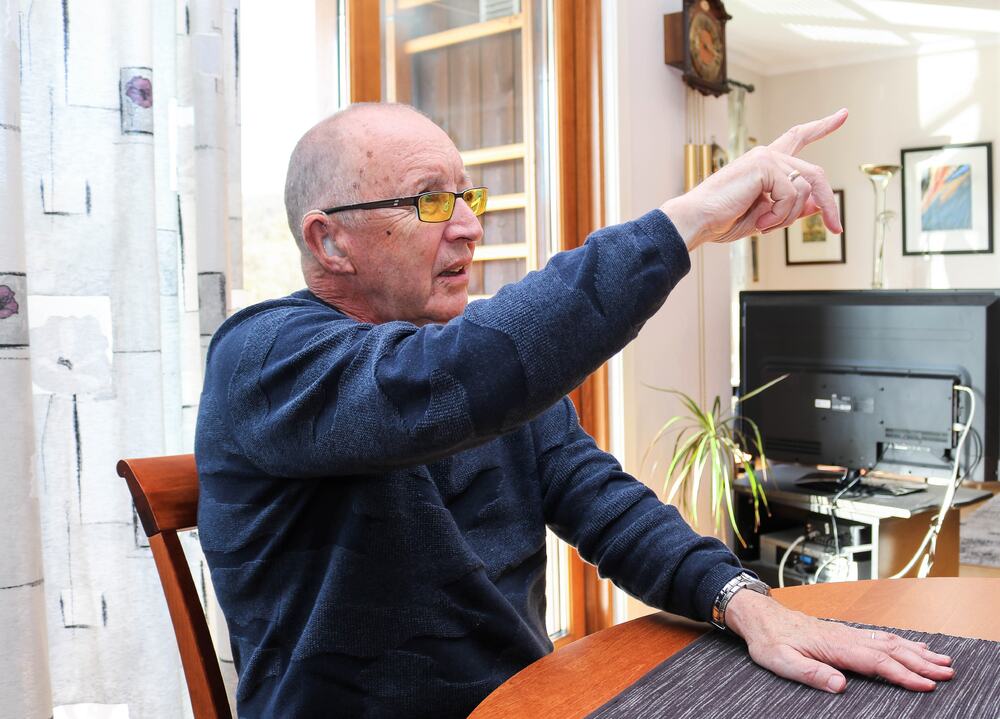 Døvblind mann med filterbriller sitter ved et spisebord og peker fremover med sin høyre hånd.