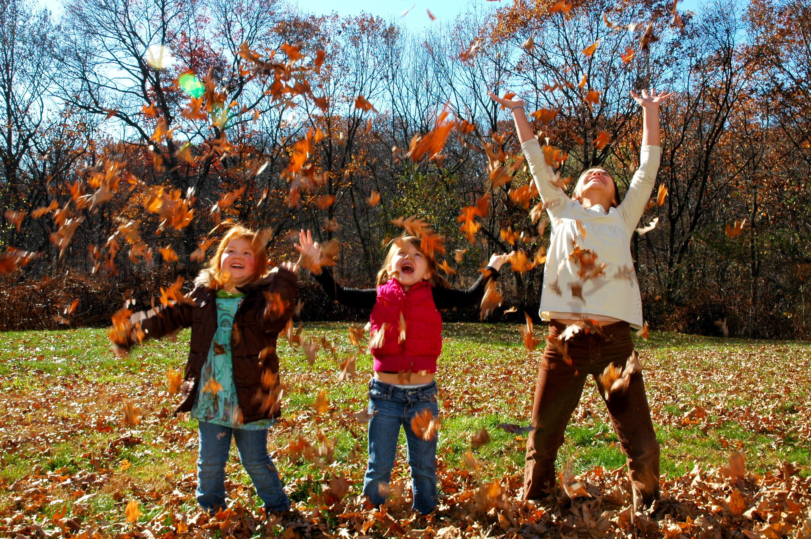 Tre barn leker med høstblader.