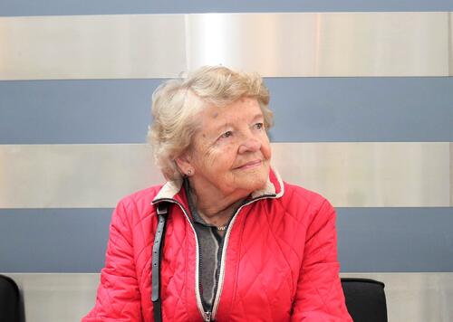 Illustrasjonsbilde av Roy-M. Østerbøl. Eldre kvinne med rød jakke ser til venstre for seg.