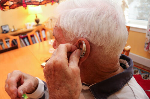 Eldre mann setter inn høreapparat i sitt venstre øre.