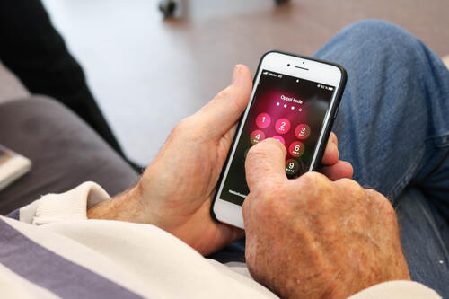 Nærbilde av eldre mann som taster inn koden sin på en iPhone.