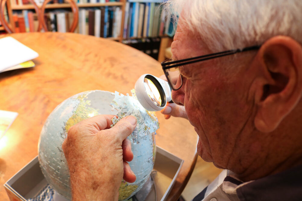 Eldre mann undersøker en puslespillbit av globus med lupe.