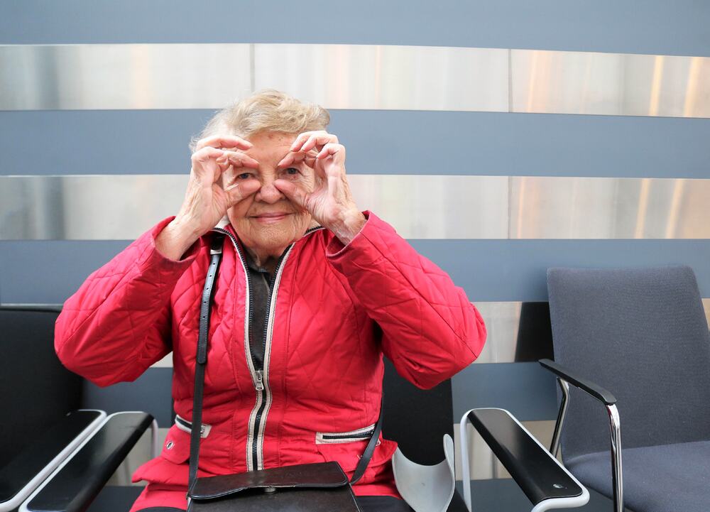 Eldre kvinne med rødjakke bruker hendene sine som "briller".