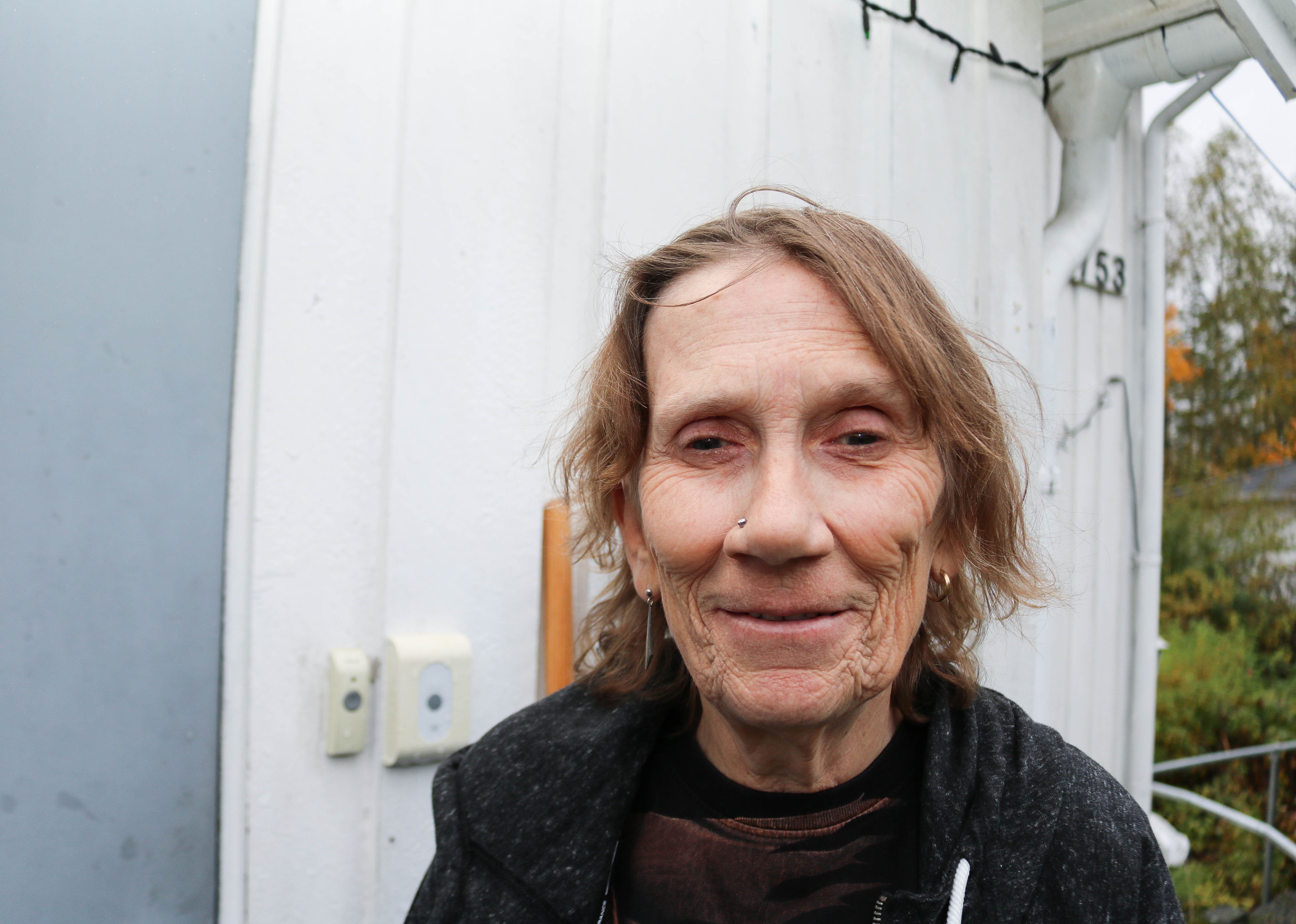 Portrettbilde av døvblind kvinne foran sin egen bolig. 