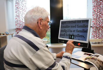 Eldre mann leser et magasin ved hjelp av forstørrelses-skjerm.