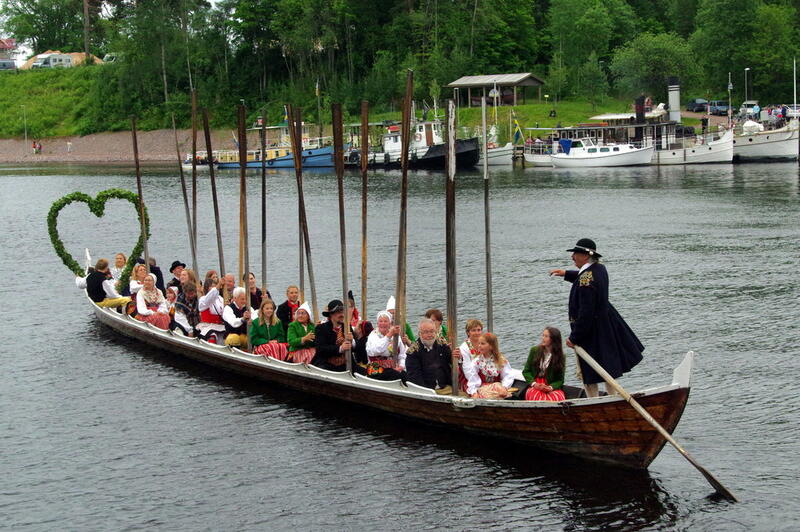 Mange personer på en båt, pyntet med blomster til midtsommerfeiring