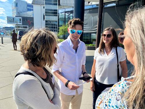 En gruppe rådgivere diskuterer utenfor inngangen til et hotell. En mann med ansikt mot fotografen har på seg solbriller med blå speilglass.