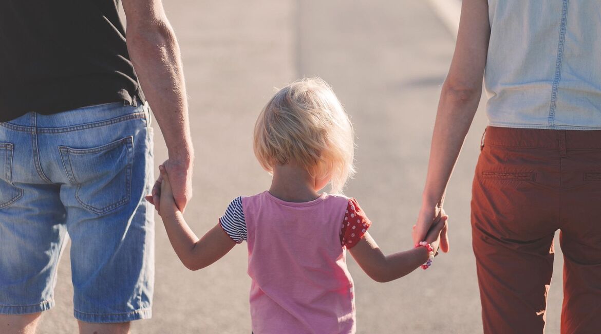 Child holding hands with its parents seen from behind
