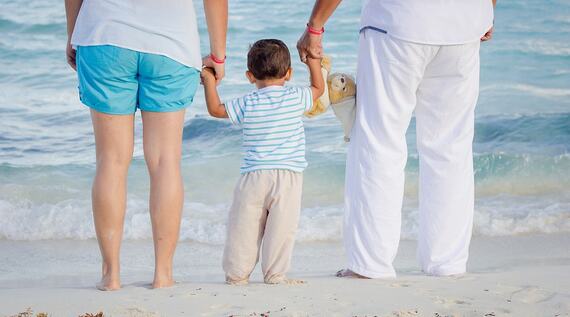 Young boy holding his parents' hands on a beach
