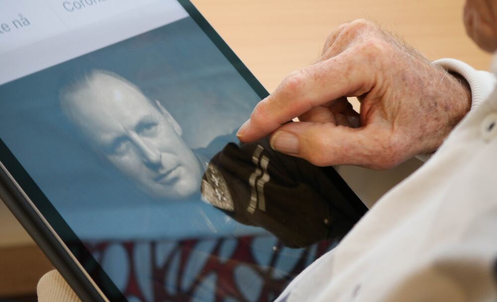 Eldre mann bruker iPad, hvor vi ser et bilde av Kong Olav i svart-hvitt.