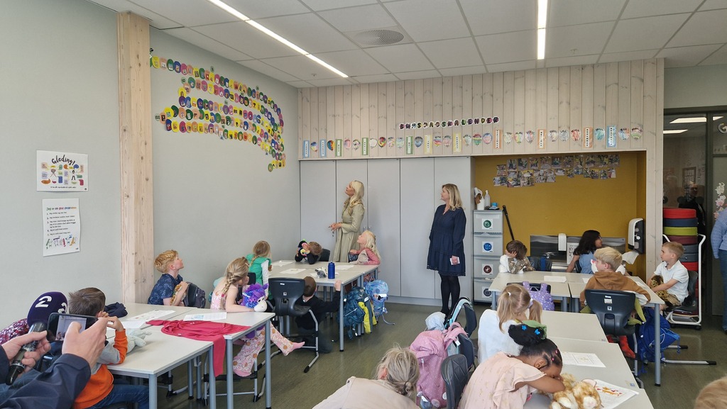Kronprinsessen leser fra plakater hengt opp på vegg, i klasserom med mange barn.