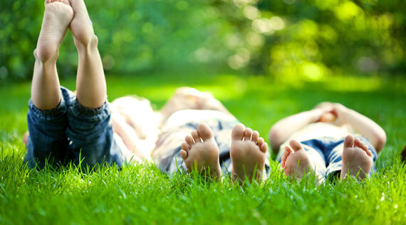 Tre barn som ligger i gresset med bare føtter