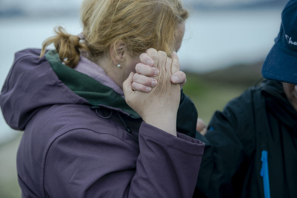 Kvinne med lilla jakke holder en manns hånd foran sitt eget ansikt.