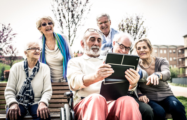 Seks eldre personer som er utendørs ser på en IPad