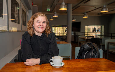 Maja Husa Jakobsen, Norges eneste fastlege med en spesialtilpasset liste for døve og personer med døvblindhet. Foto: Sigve Nedredal. Kvinne med brunt hår med svart trøye sitter ved et bord med en hvit kopp foran henne.